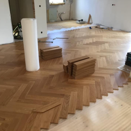 Tømrerarbejde med sildebensparketgulv under installation.