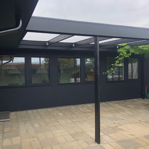 Tømrerarbejde på en sort facade med glasoverdækket terrasse.