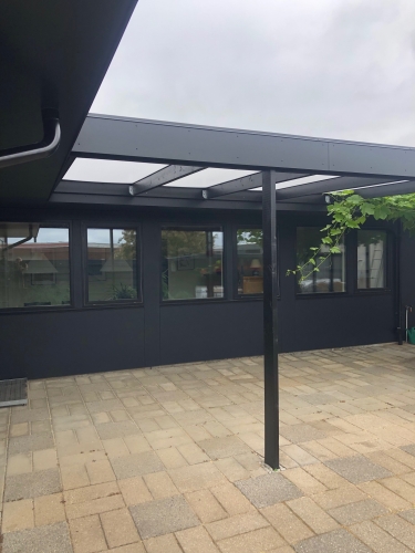 Tømrerarbejde på en sort facade med glasoverdækket terrasse.